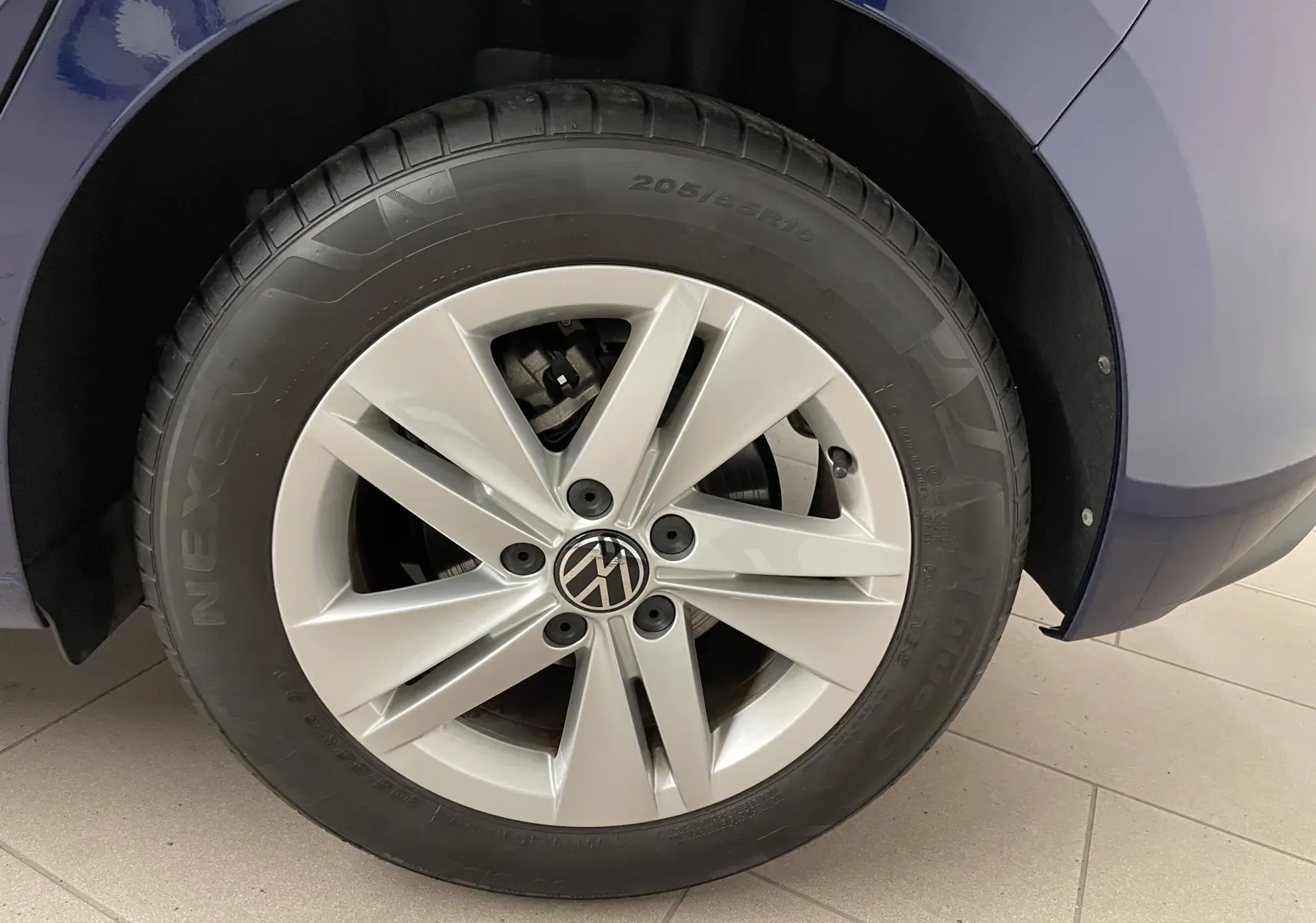 Gros plan sur la roue avant droite d'une Volkswagen Golf 2023 Bleu Atlantique avec jante argentée et logo VW.