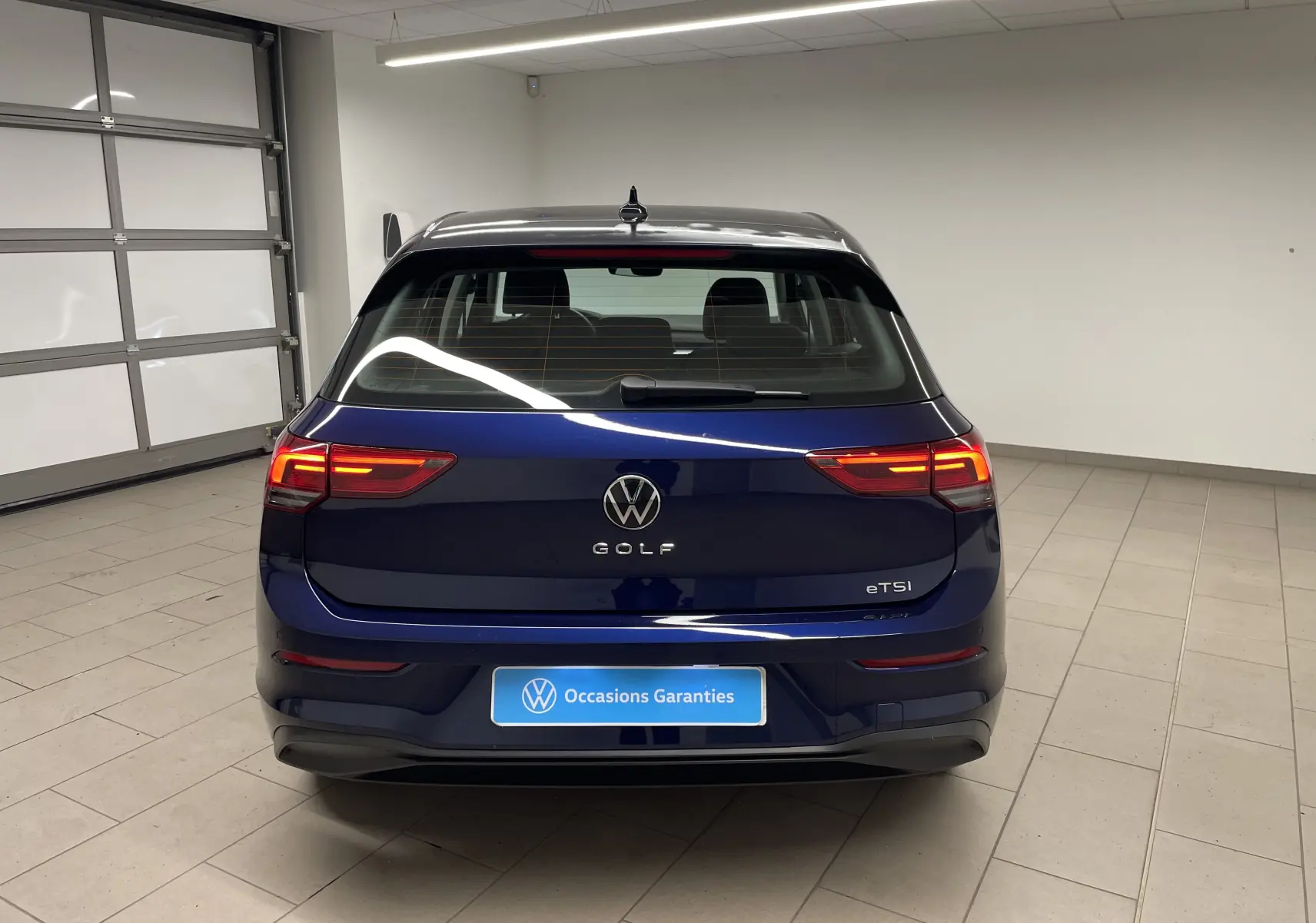 Vue arrière d'une Volkswagen Golf 1.0 TSI 110 DSG7 Life Plus 2023 en bleu Atlantique métallisé avec feux allumés.
