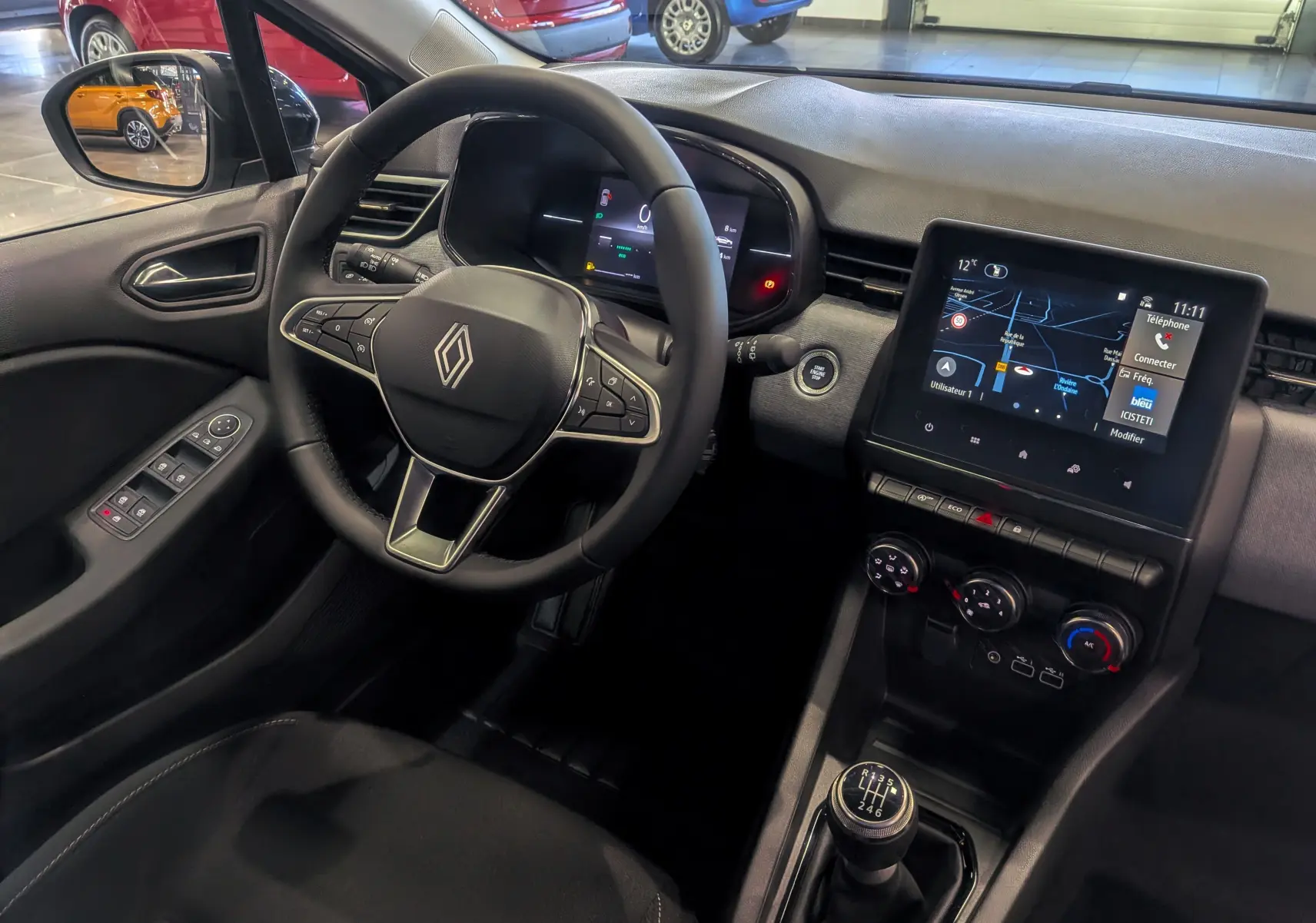 Vue intérieure côté conducteur de la Renault Clio V gris Rafale, avec volant multifonctions et écran tactile central allumé.