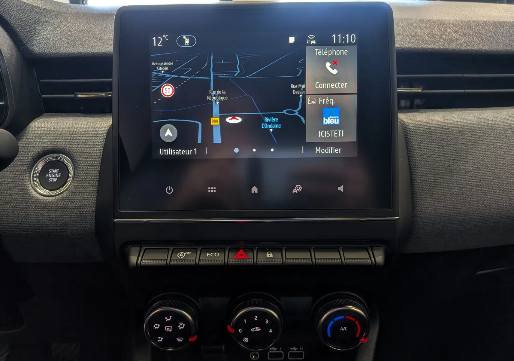 Vue rapprochée de l’écran tactile central et des commandes de climatisation du Renault Clio V Gris Rafale, intérieur noir.