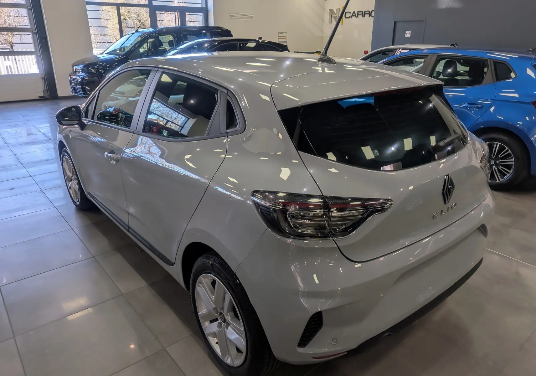 Vue 3/4 arrière droite d'une Renault Clio V gris Rafale en intérieur, avec feux arrière LED et caméra de recul visible.
