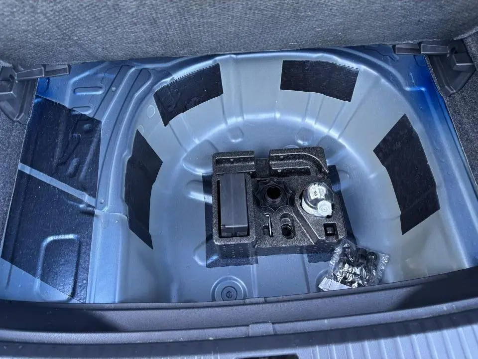 Vue plongeante sur le coffre ouvert du SEAT Arona bleu saphir, montrant le rangement sous plancher sans roue de secours.