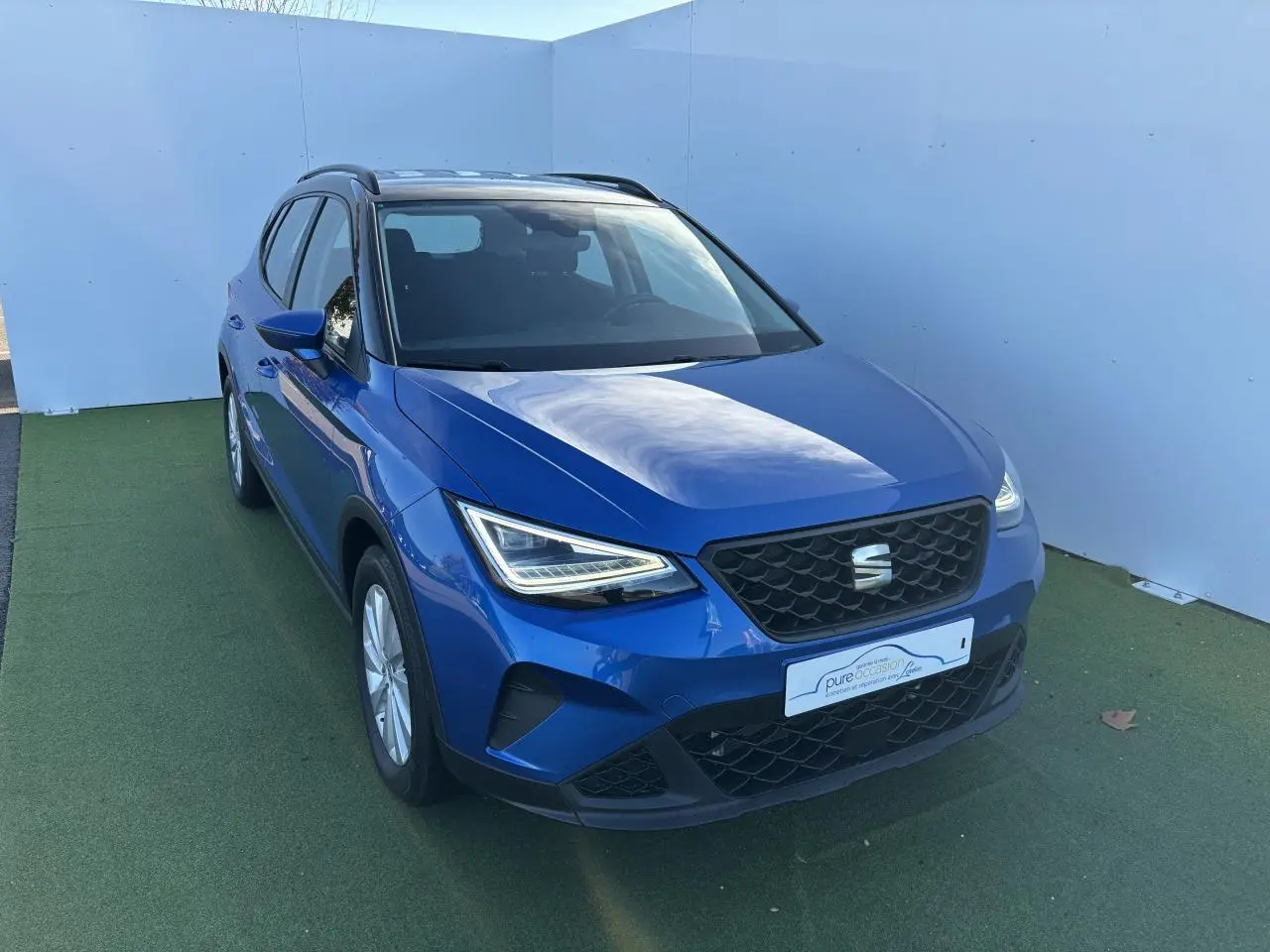 Vue 3/4 avant d'un SEAT Arona bleu saphir avec toit noir, calandre noire et jantes alliage 16 pouces.