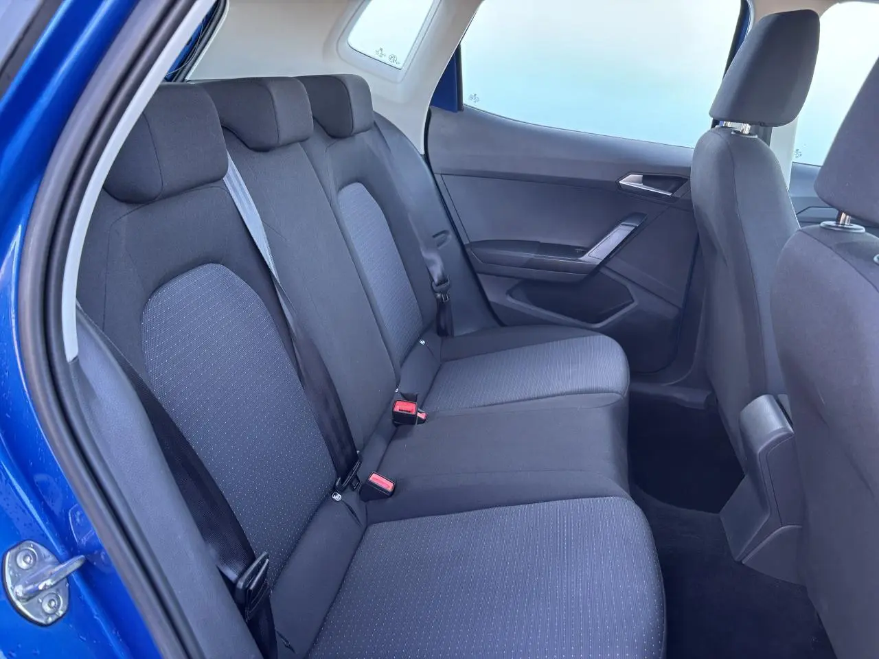 Vue intérieure côté arrière droit du SEAT Arona bleu saphir, montrant la banquette arrière en tissu noir.