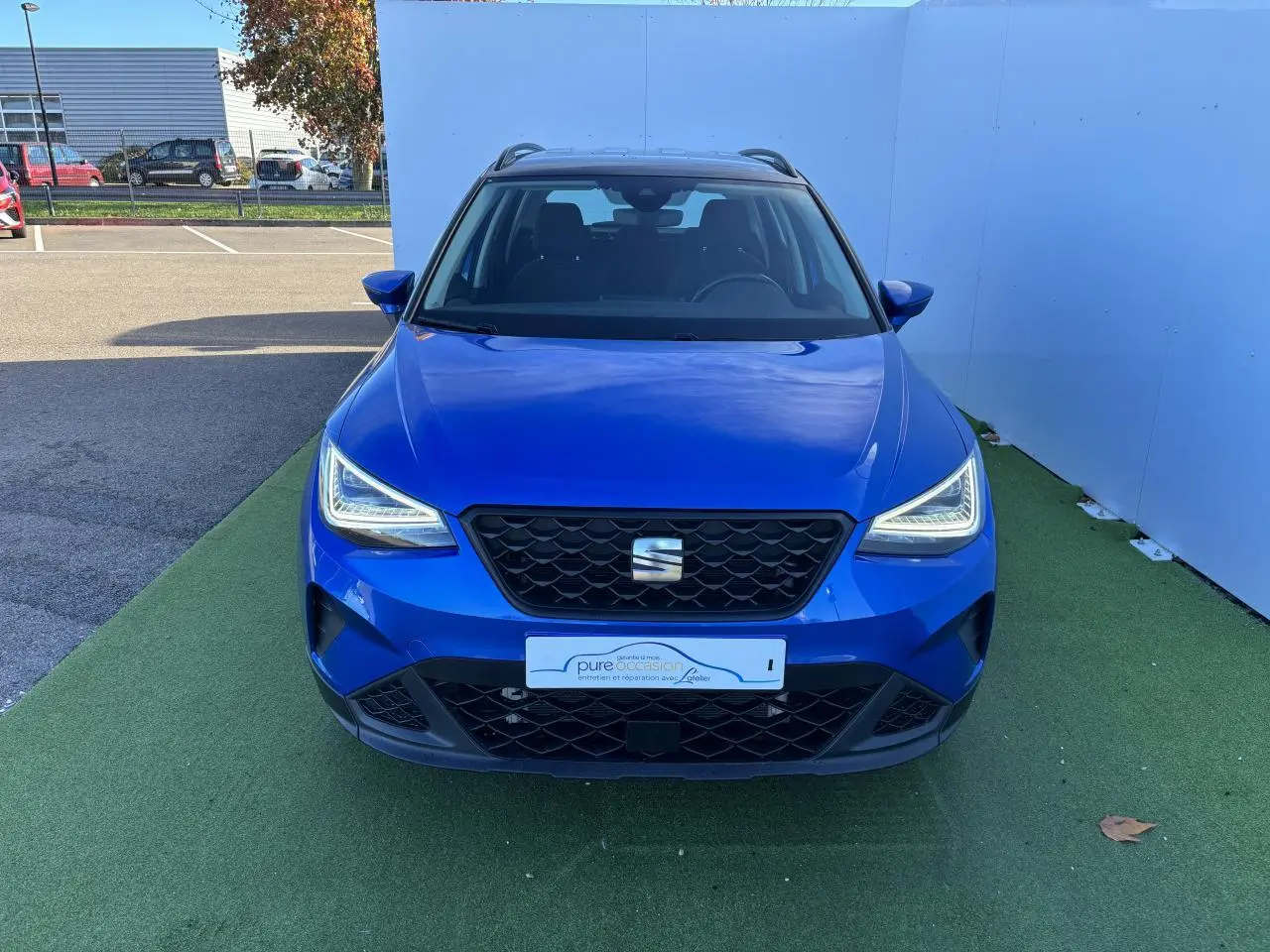 Vue frontale d'un SEAT Arona bleu saphir avec toit noir, phares LED allumés et calandre noire distinctive.