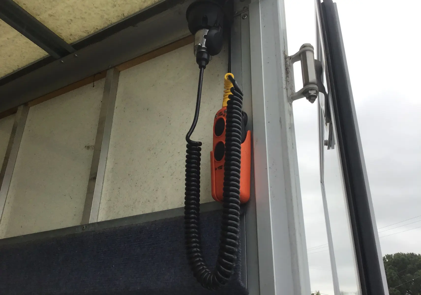 Détail intérieur du hayon électrique d’un Opel Movano blanc, montrant la commande suspendue orange avec câble spiralé.