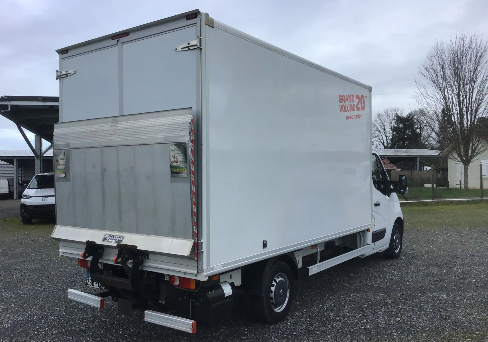 Vue 3/4 arrière droite d’un utilitaire blanc Opel Movano Châssis Cabine avec hayon élévateur et marquage "Grand Volume 20m3".