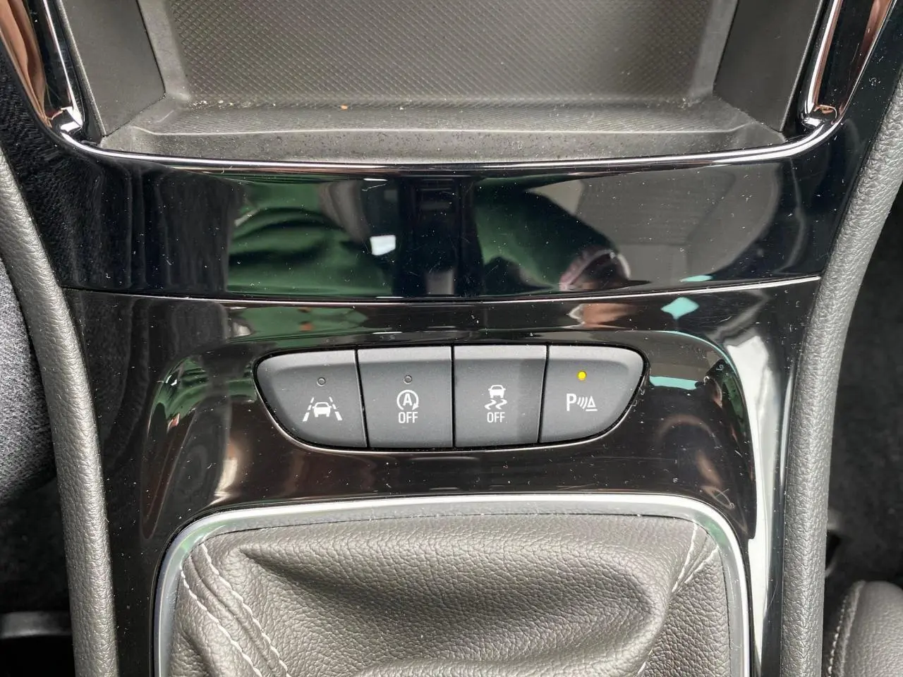 Gros plan sur la console centrale noire brillante de l'Opel Astra 2021, avec boutons d'aide au stationnement et levier de vitesse.