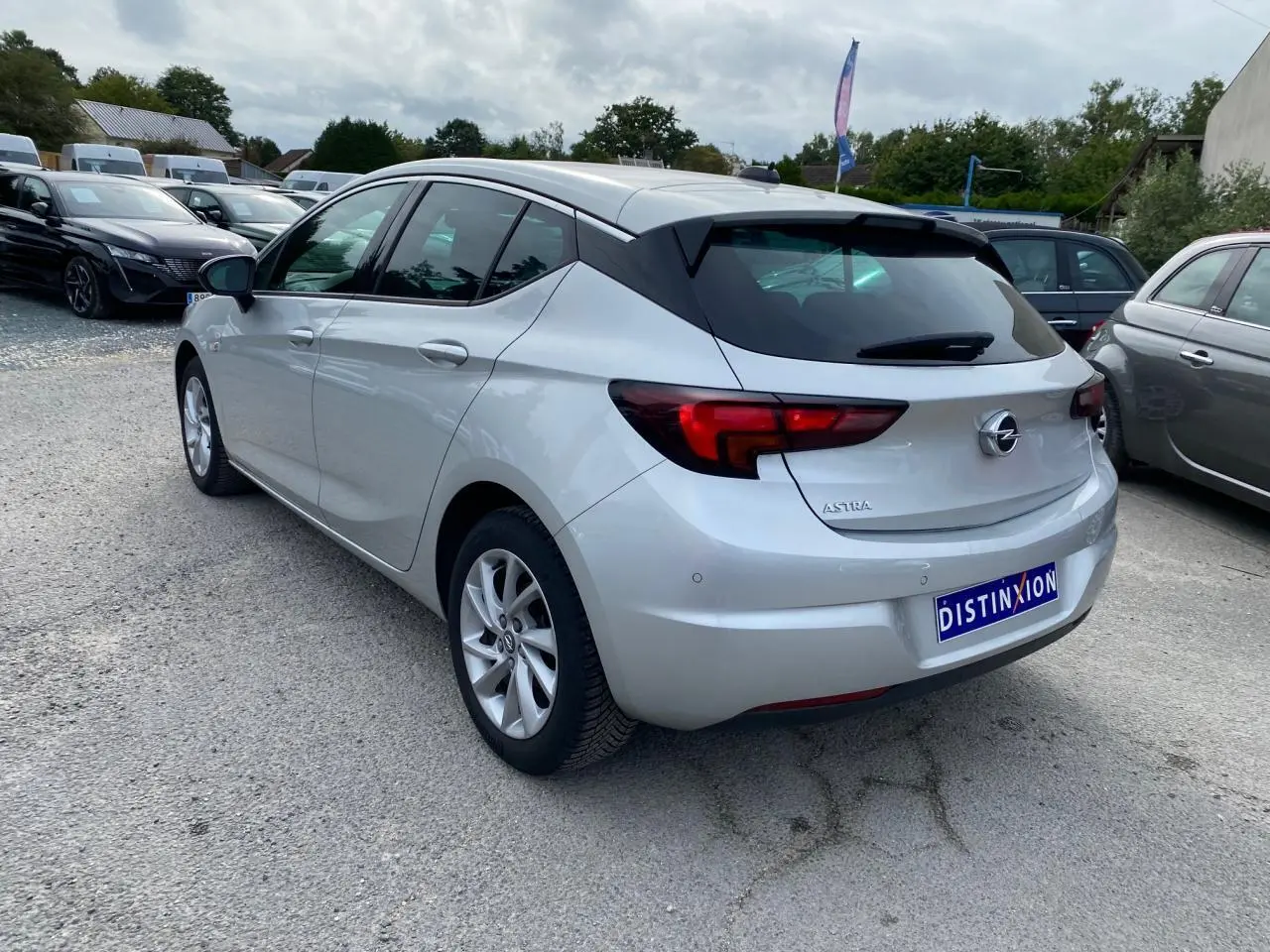 Opel Astra 2021 couleur argent vue 3/4 arrière droit avec vitres surteintées et jantes alliage 16 pouces.