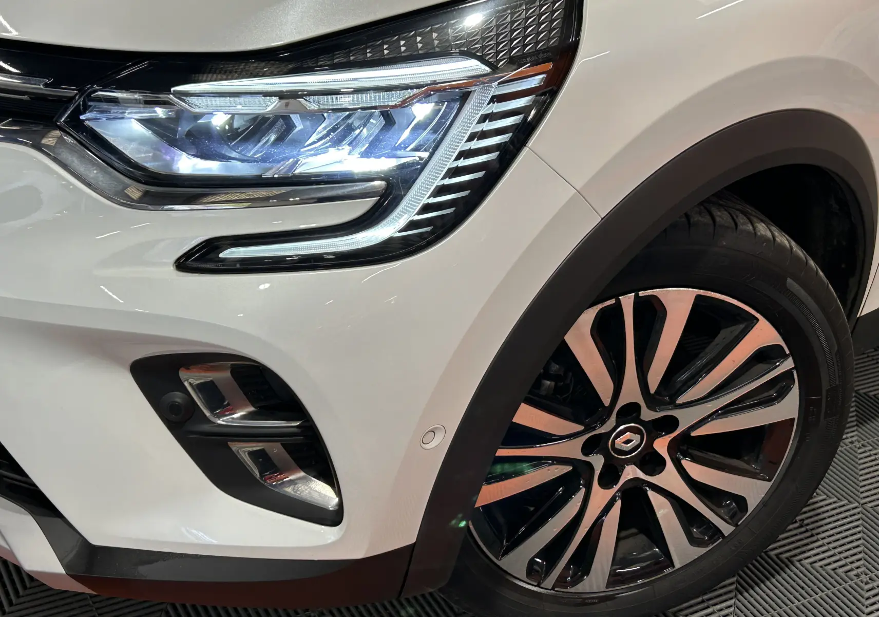 Gros plan sur l'avant droit blanc nacré du Renault Captur II Iconic, mettant en valeur le phare LED et la jante bi-ton.