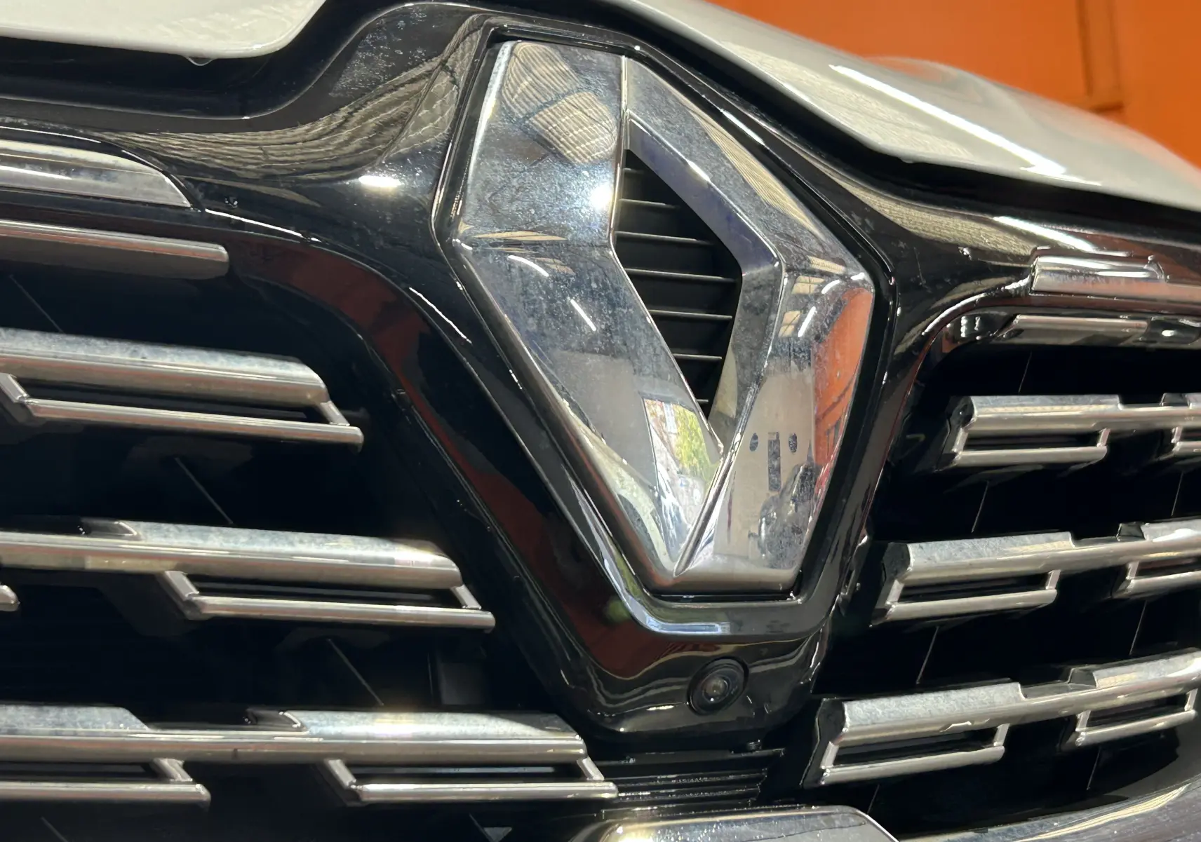 Gros plan sur la calandre noire et chromée du Renault Captur blanc nacré avec logo et caméra 360° intégrée.