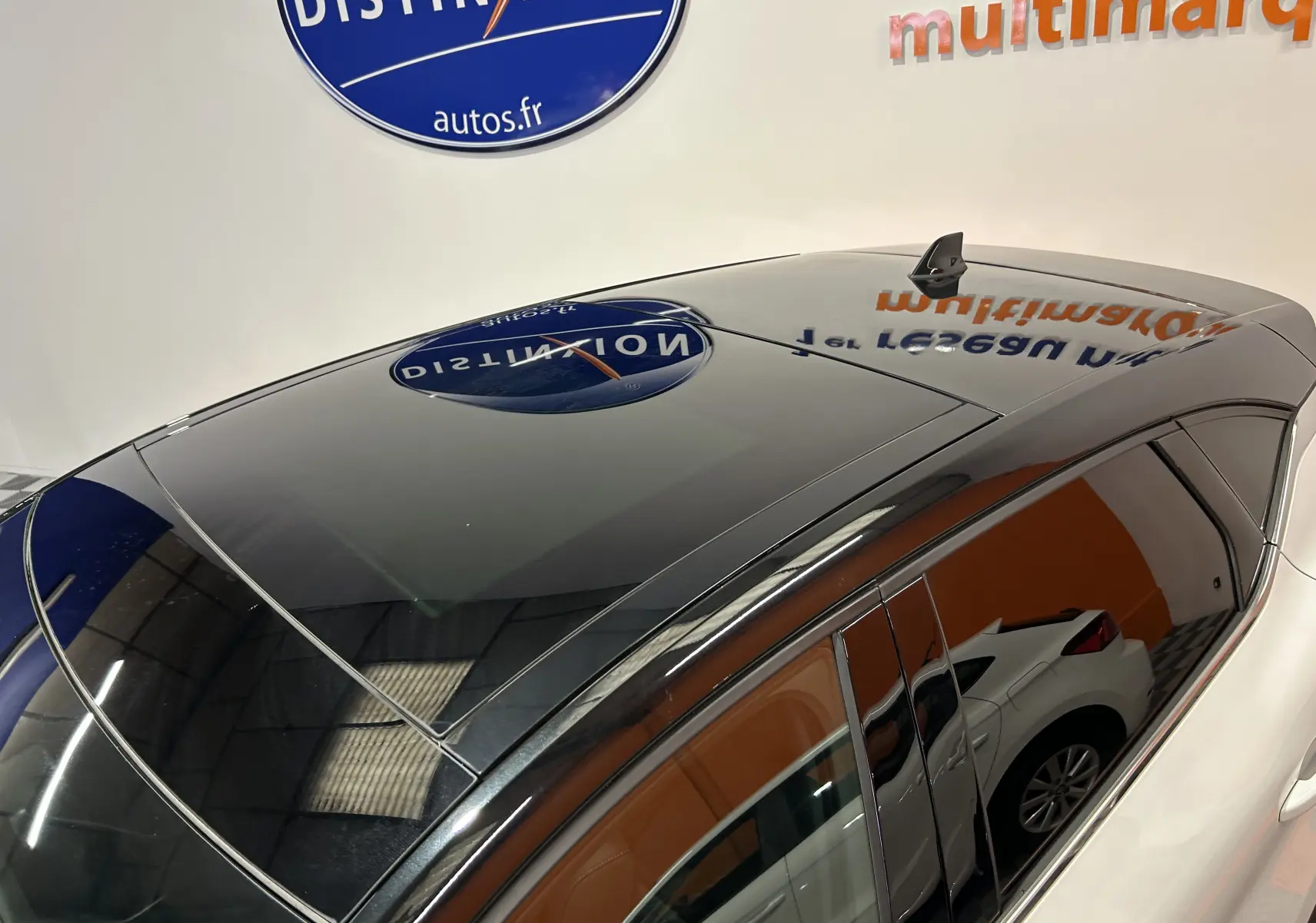 Toit ouvrant panoramique noir brillant du Renault Captur blanc nacré vu de dessus côté gauche, reflet d'enseigne visible.