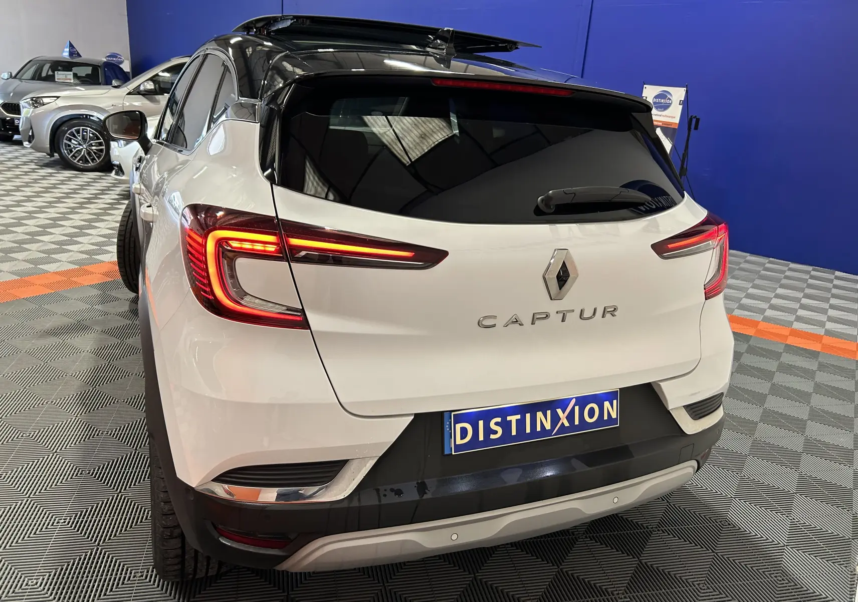 Vue 3/4 arrière d’un Renault Captur blanc nacré avec toit noir et feux arrière allumés en intérieur showroom.