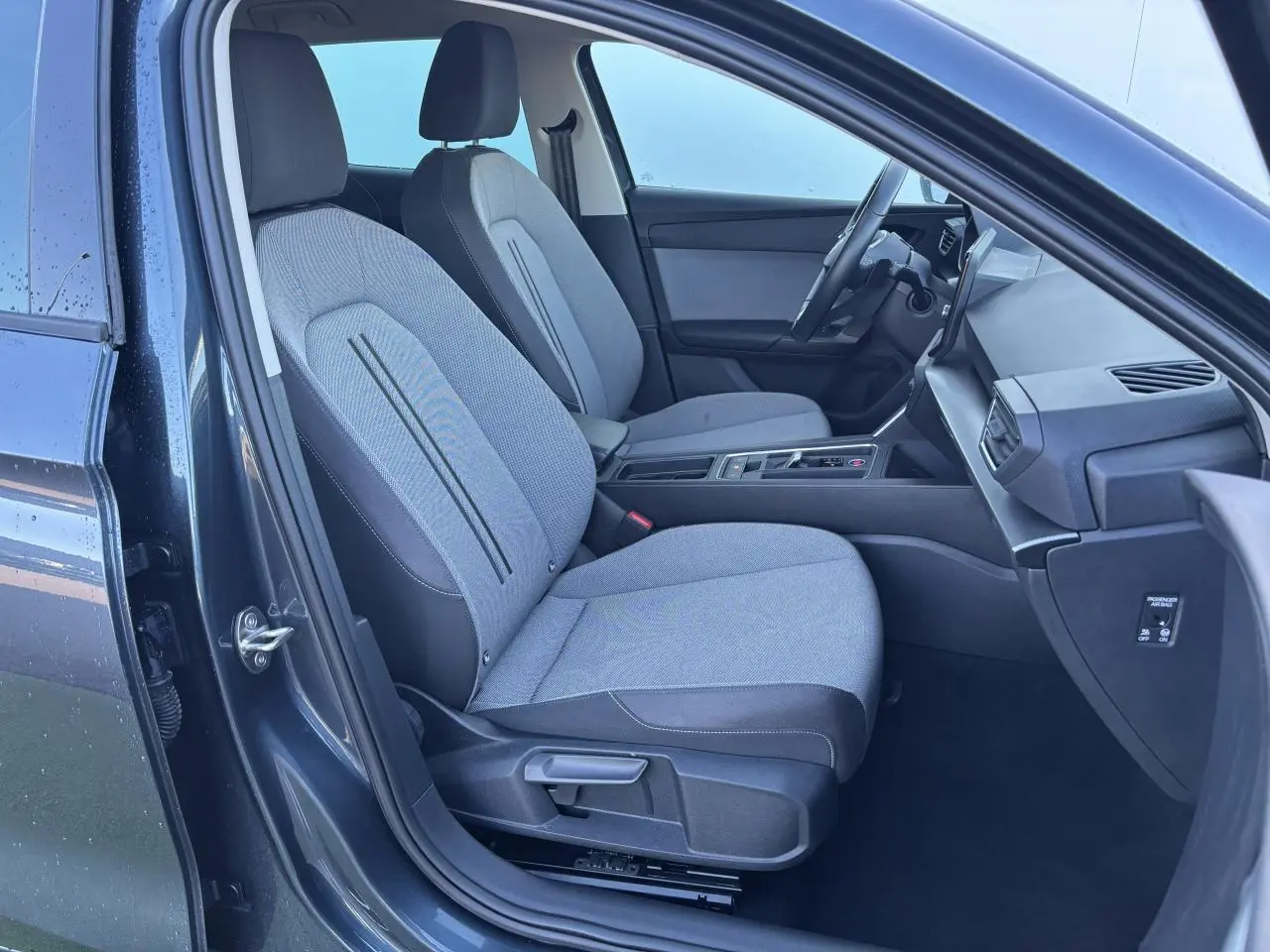 Vue intérieure côté gauche de la SEAT LEON IV gris magnetic, montrant les sièges avant et la console centrale moderne.