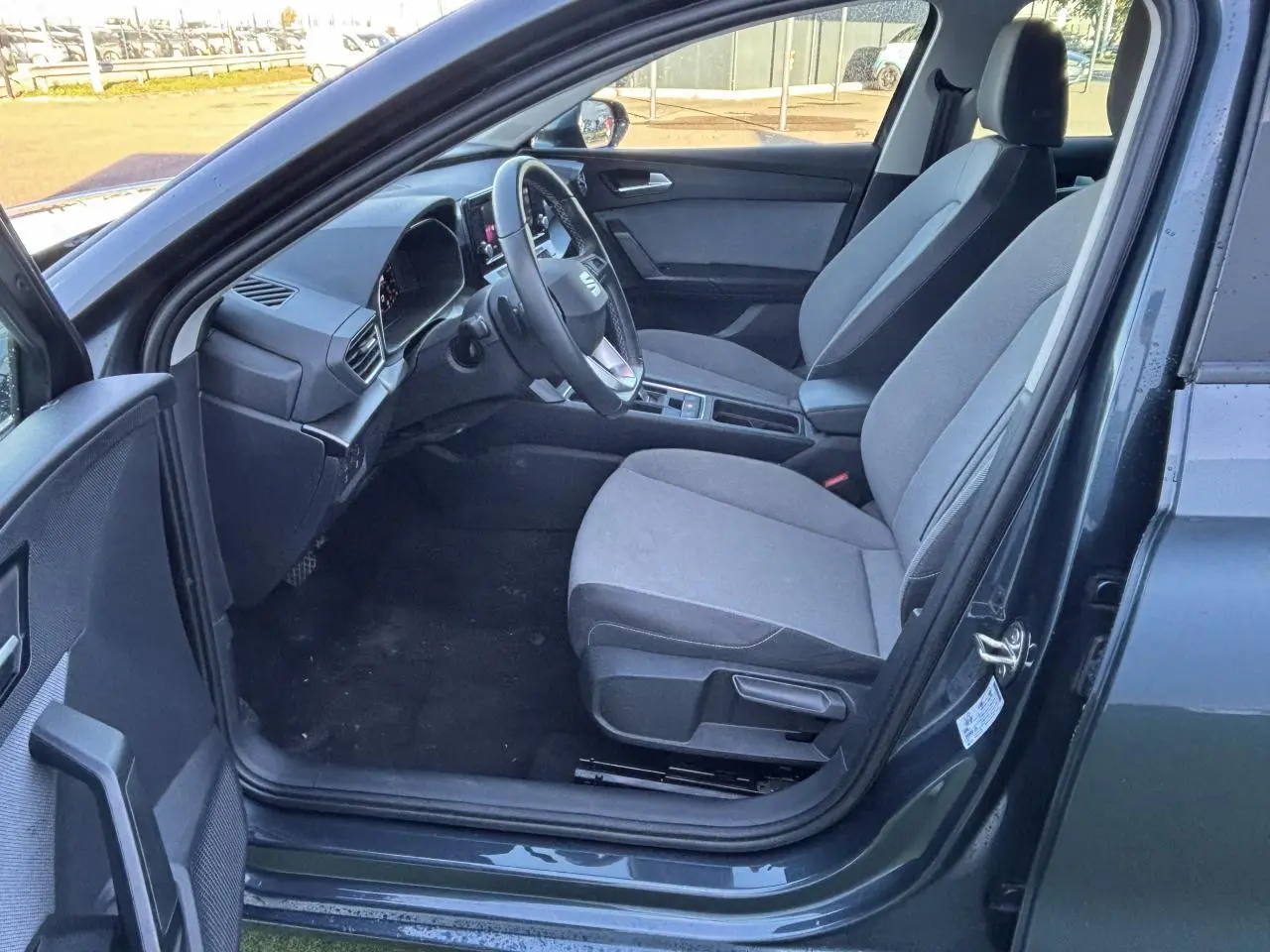 Intérieur côté conducteur d'une SEAT Leon gris magnetic 2024, montrant sièges tissu et tableau de bord moderne.