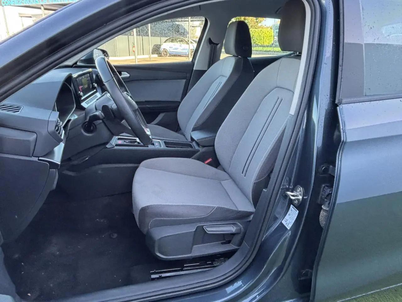 Vue intérieure côté conducteur de la SEAT LEON IV gris magnetic, montrant les sièges tissu et le volant multifonction cuir.