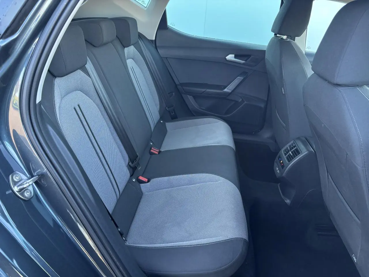 Vue intérieure côté arrière gauche du SEAT Leon gris magnetic, montrant la banquette arrière bicolore et les aérateurs centraux.