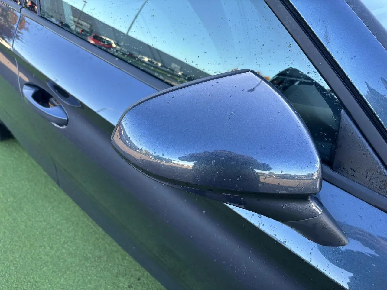 Rétroviseur côté gauche gris magnetic d'une SEAT Leon 2024 avec portière et poignée visibles sous la pluie.