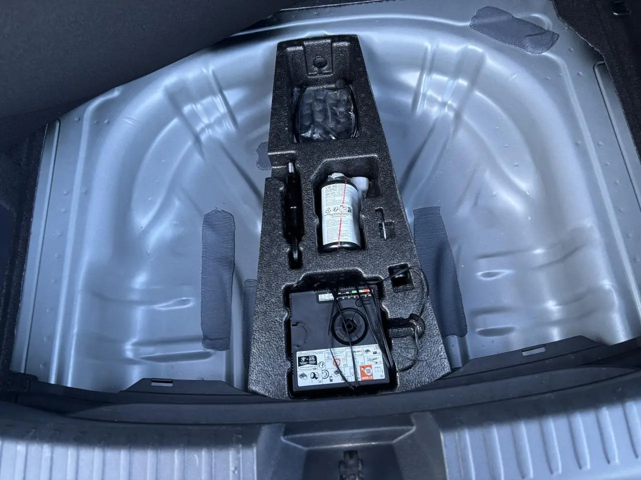 Vue plongeante sur le coffre ouvert d'une SEAT LEON gris magnetic, montrant le rangement pour roue de secours et kit de réparation.
