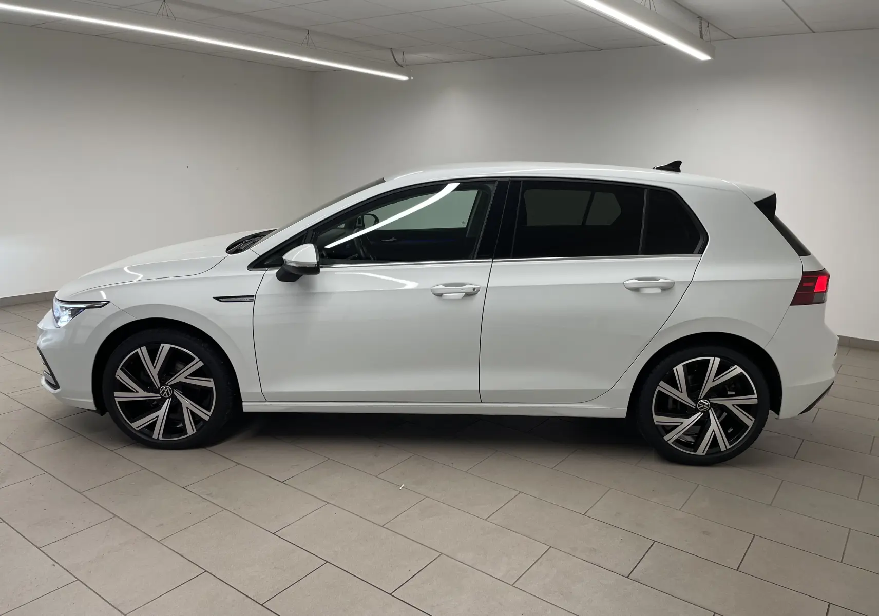 Profil côté gauche d'une Volkswagen Golf 1.5 eTSI Style blanche avec jantes Bergamo et vitres arrière surteintées.