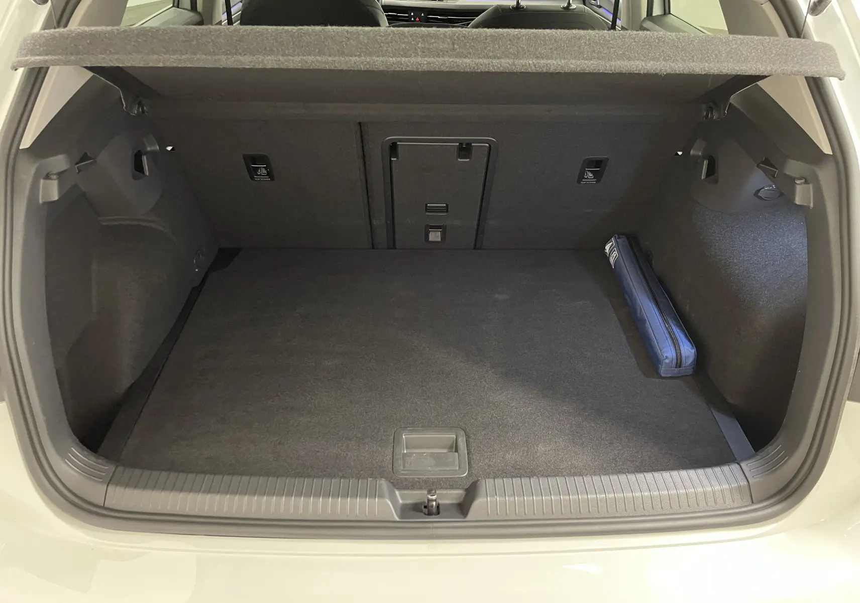 Coffre ouvert d'une Volkswagen Golf blanche, vue arrière montrant un espace de chargement propre avec trousse bleue sur le côté droit.