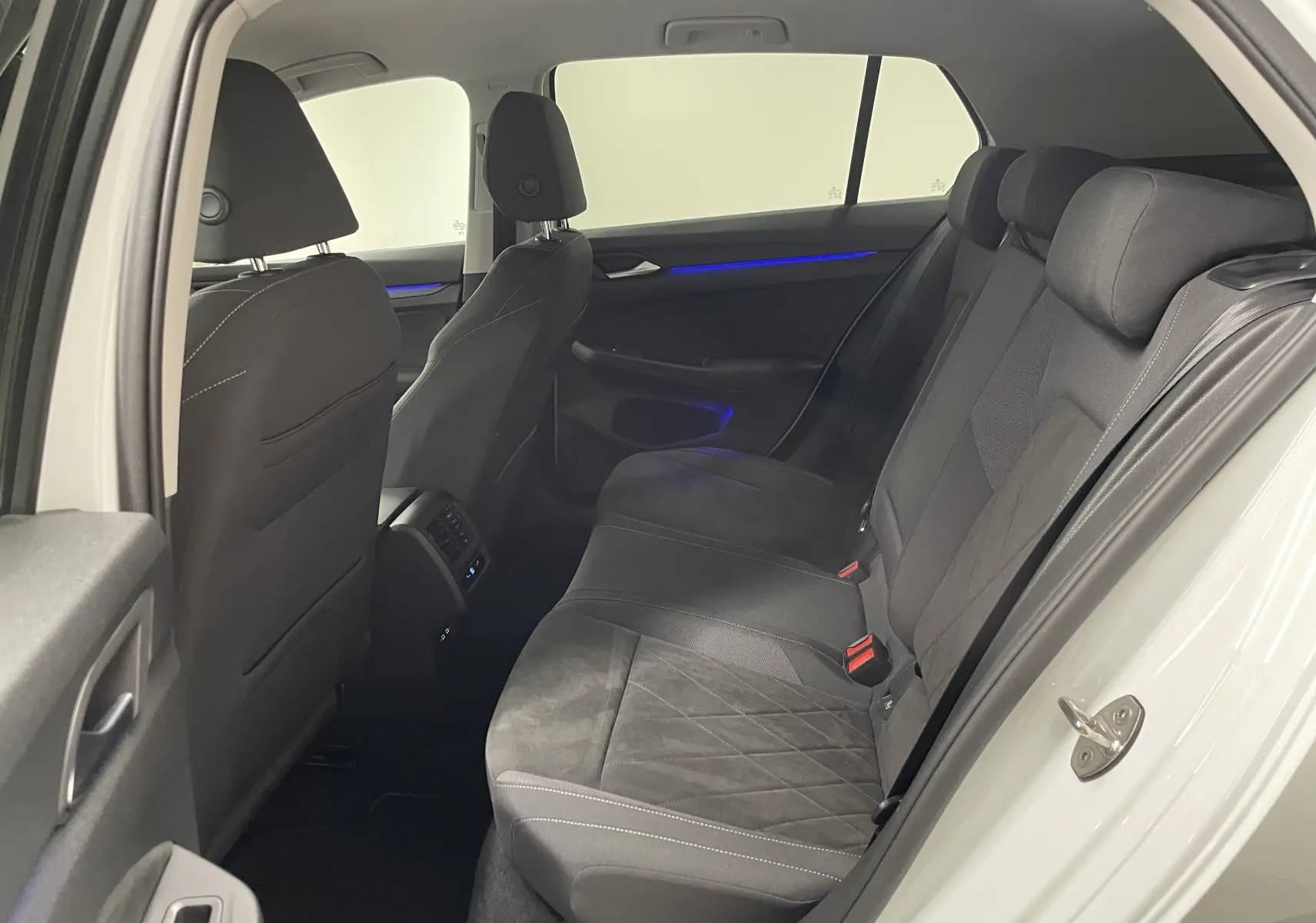 Vue intérieure côté gauche sur les sièges arrière noirs et l'éclairage d'ambiance bleu d'une Volkswagen Golf blanche 2023.