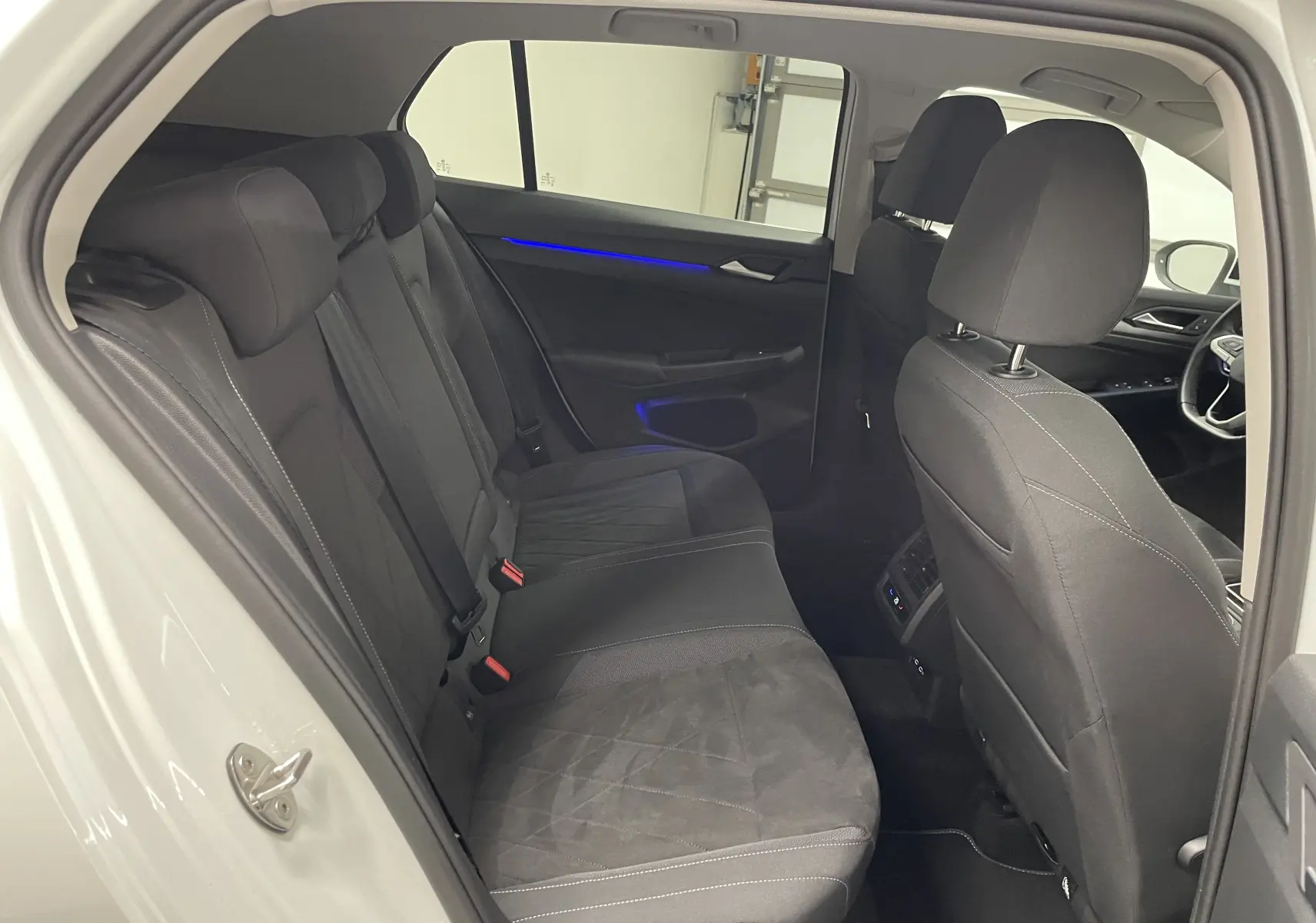 Vue intérieure arrière côté gauche de la Volkswagen Golf 1.5 eTSI Style 2023 avec sièges noirs et éclairage d'ambiance bleu.