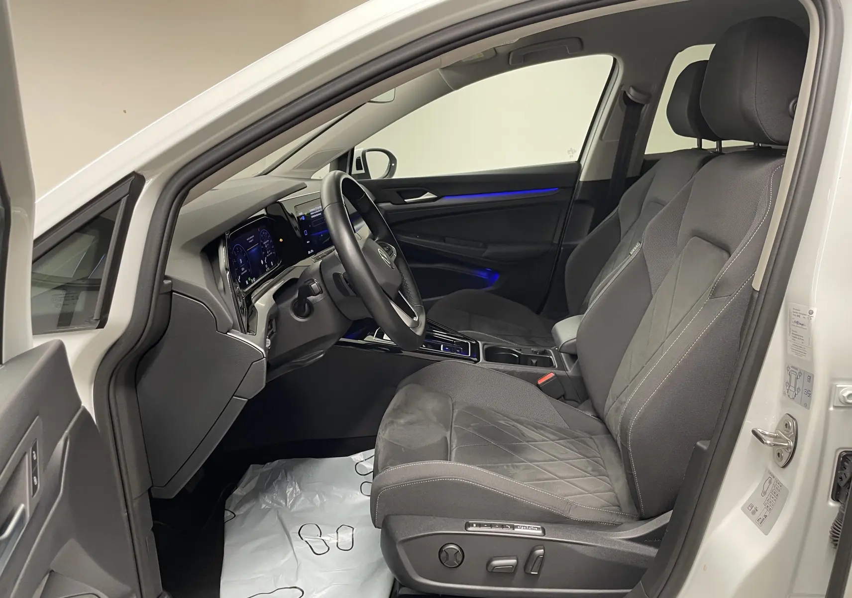 Intérieur avant droit d'une Volkswagen Golf blanche 2023, sièges noirs avec surpiqûres et éclairage d'ambiance bleu