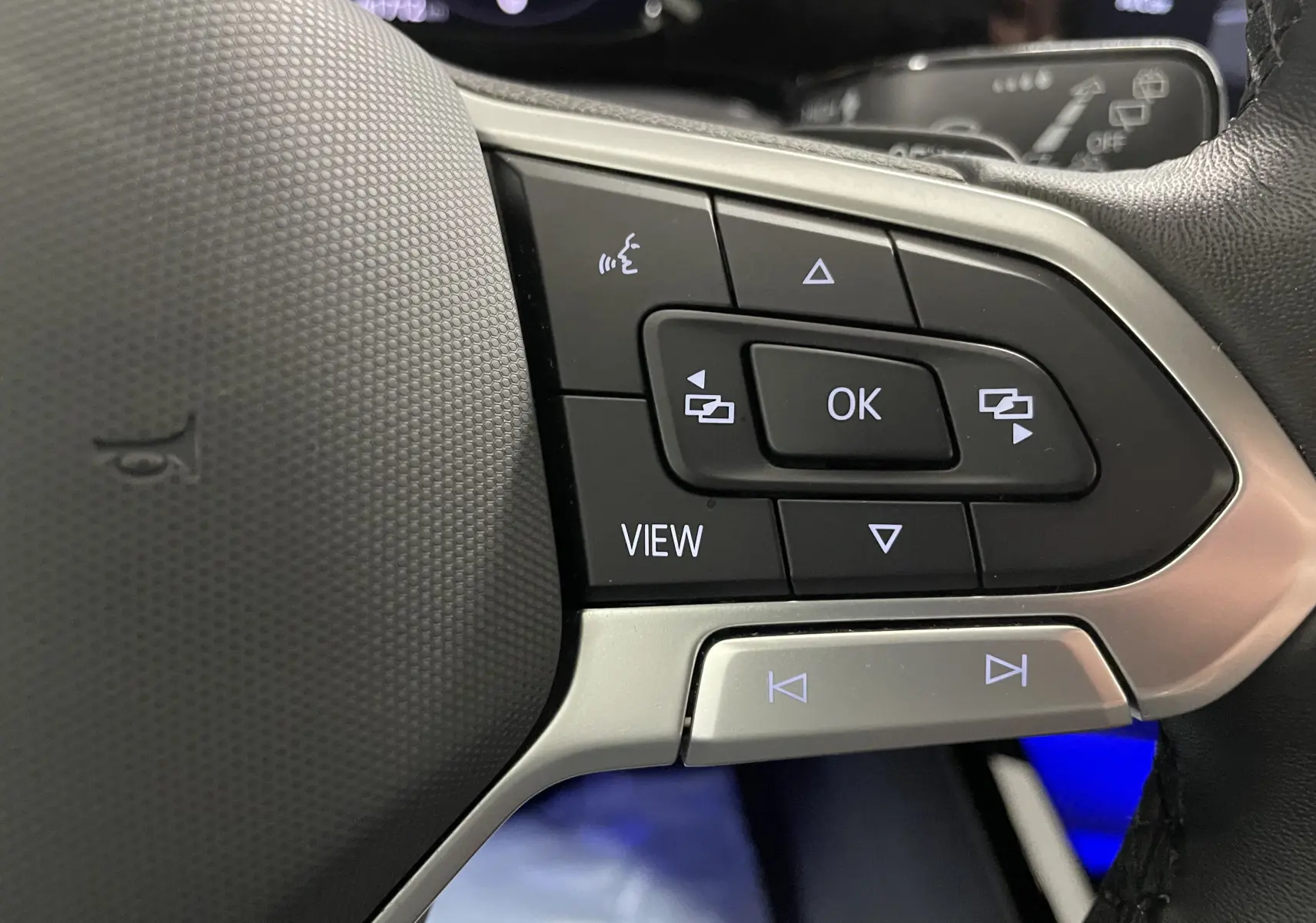 Gros plan sur les commandes multifonctions à droite du volant d'une Volkswagen Golf blanche, avec boutons rétroéclairés.