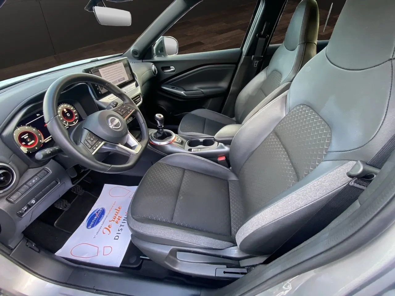 Vue intérieure côté conducteur du Nissan Juke 2025, sièges tissu noir et tableau de bord digital moderne.