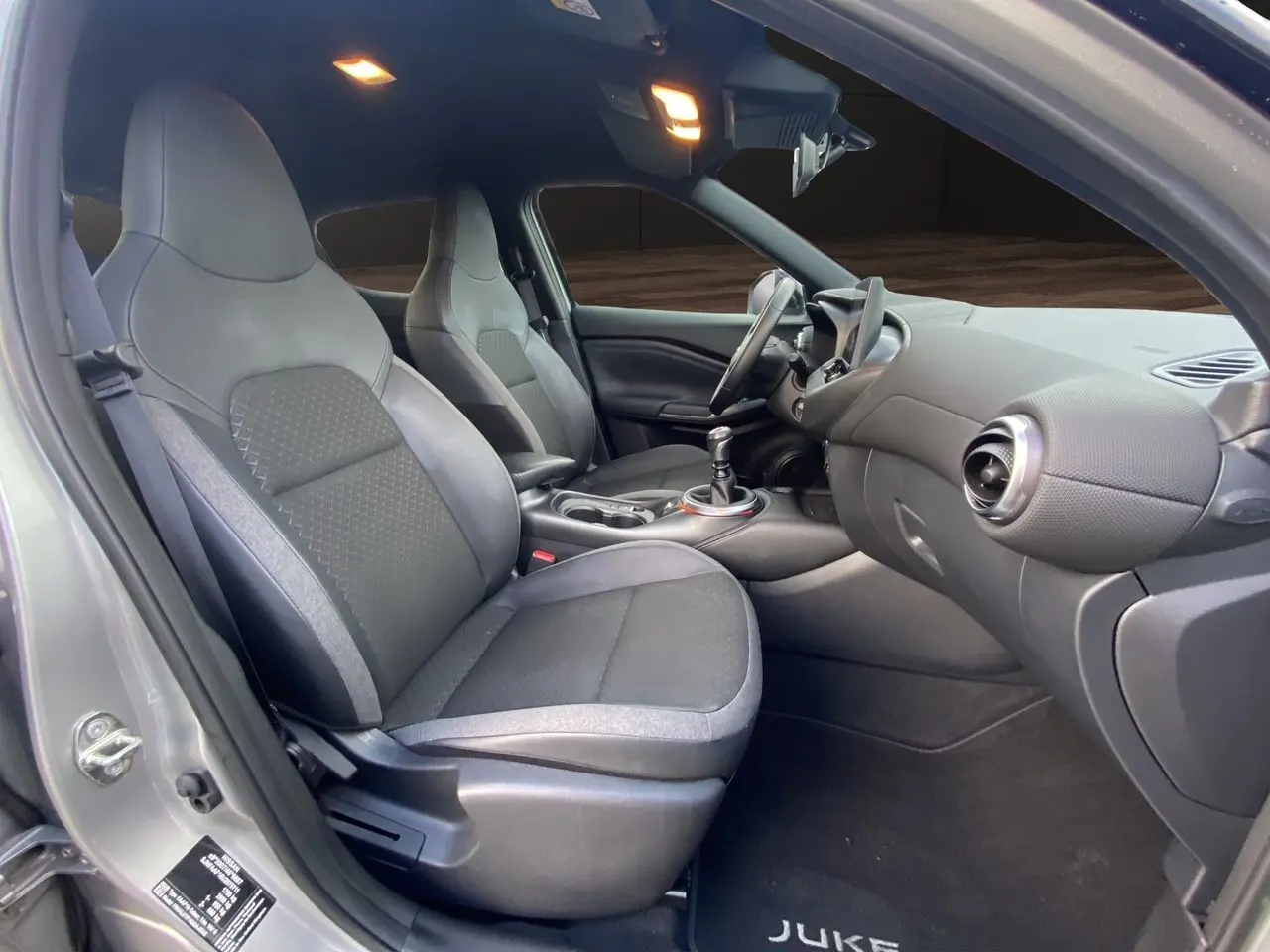 Vue intérieure côté gauche du Nissan Juke 2025, sièges tissu noir avec cuir synthétique et tableau de bord moderne.