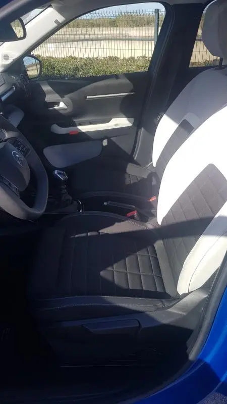 Vue intérieure côté conducteur de la Citroën C3 bleu foncé 2024, sièges bicolores noirs et blancs, volant et levier de vitesses visibles.