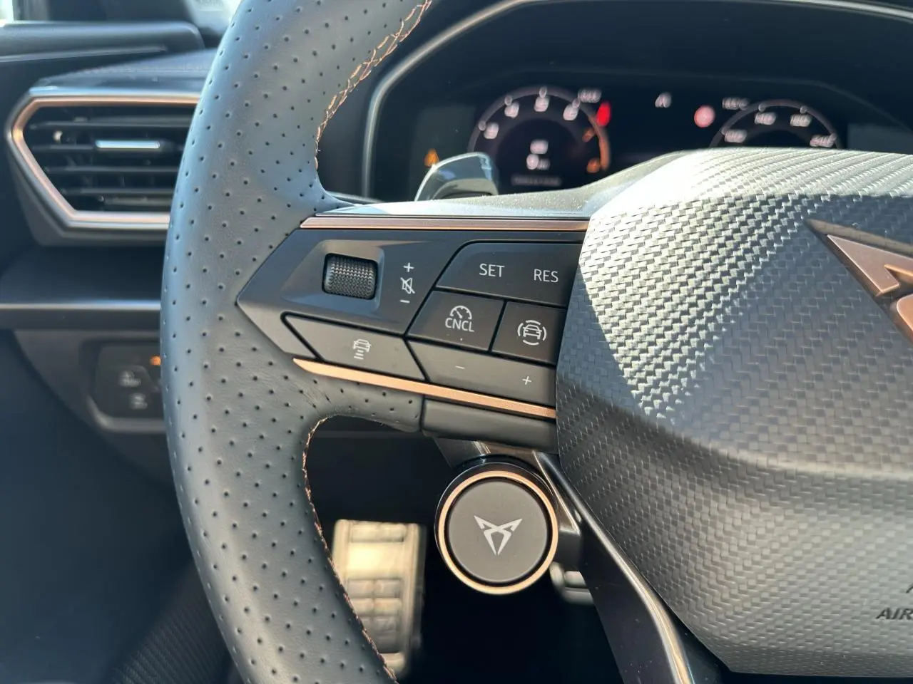 Gros plan sur le volant perforé noir avec logo CUPRA et commandes multifonctions dans l'habitacle du Leon Sportstourer.