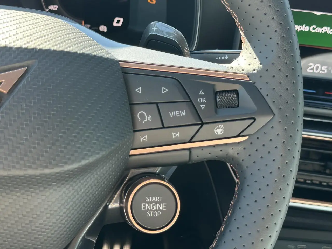 Gros plan sur le volant perforé noir avec commandes et bouton Start Engine Stop du CUPRA Leon Sportstourer gris magnétique.