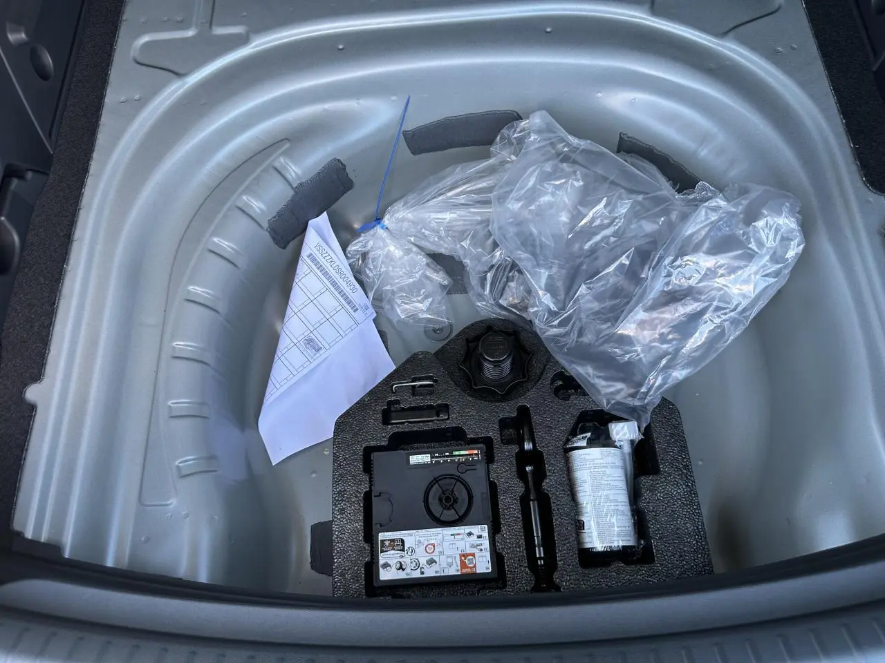 Gros plan sur le coffre ouvert d'une CUPRA Leon Sportstourer gris magnétique, montrant la roue de secours et les outils rangés.