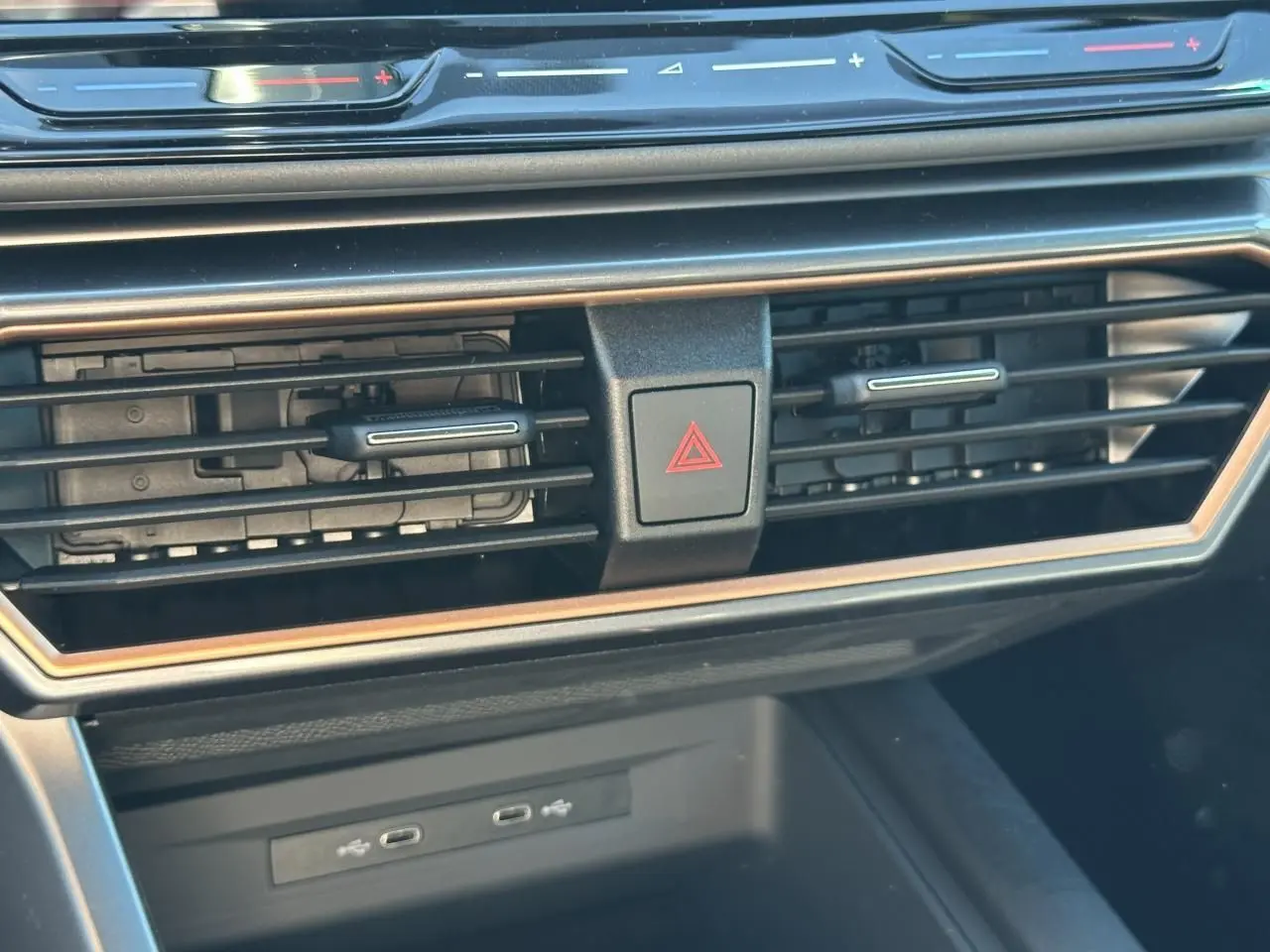 Gros plan sur la console centrale du CUPRA Leon Sportstourer 2025, avec aérateurs noirs et cadre cuivré, boutons tactiles rouges.