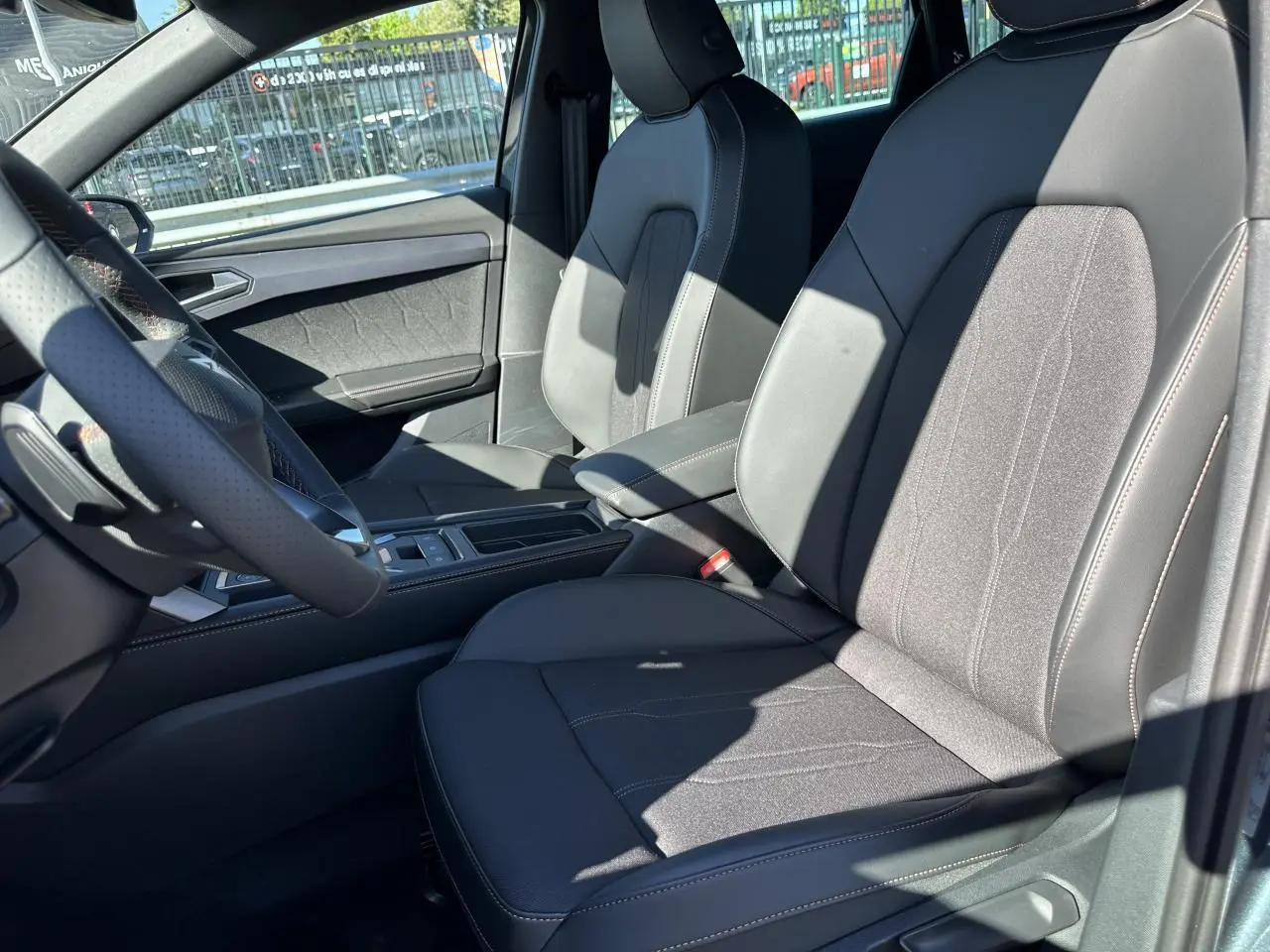 Intérieur de la CUPRA Leon Sportstourer 2025, vue côté conducteur sur sièges sports bimatière noirs et accoudoir central.