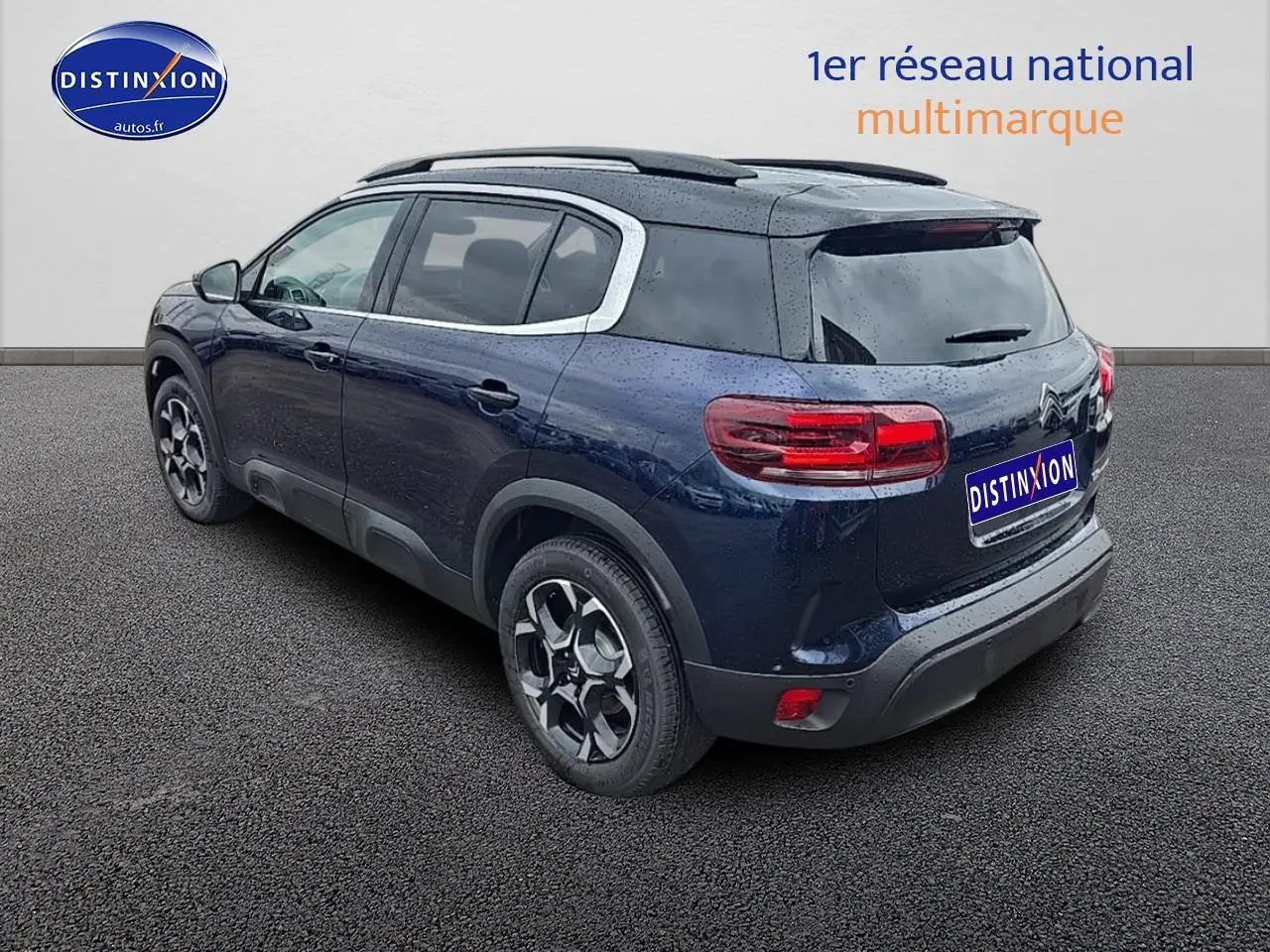Vue 3/4 arrière droite d'un Citroën C5 Aircross bleu eclipse avec jantes alliage et barres de toit noires.