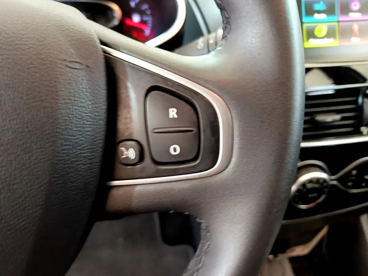 Gros plan sur le volant cuir noir de la Renault Clio Business TCe 90 avec commandes audio et tableau de bord partiellement visible.