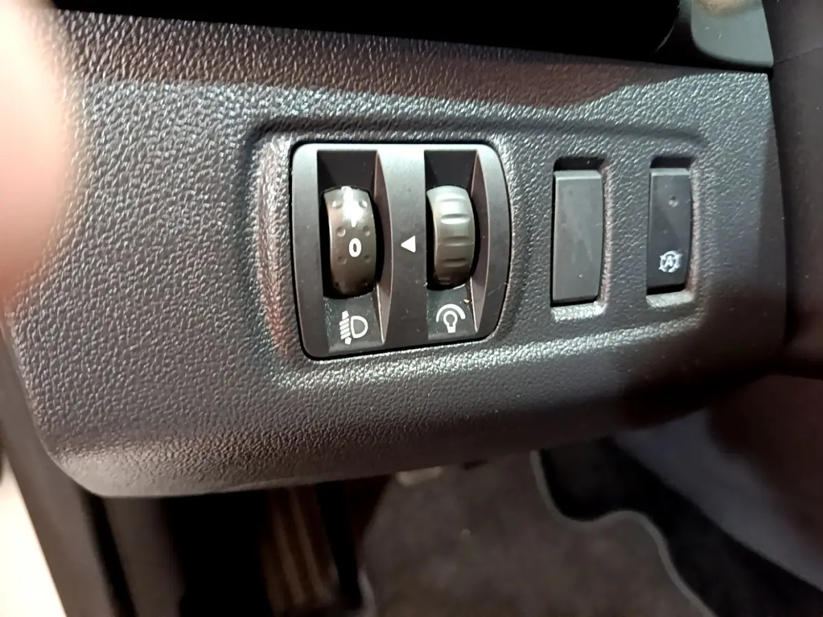 Gros plan sur les commandes de réglage des phares et de luminosité du tableau de bord dans une Renault Clio Business blanche de 2019.