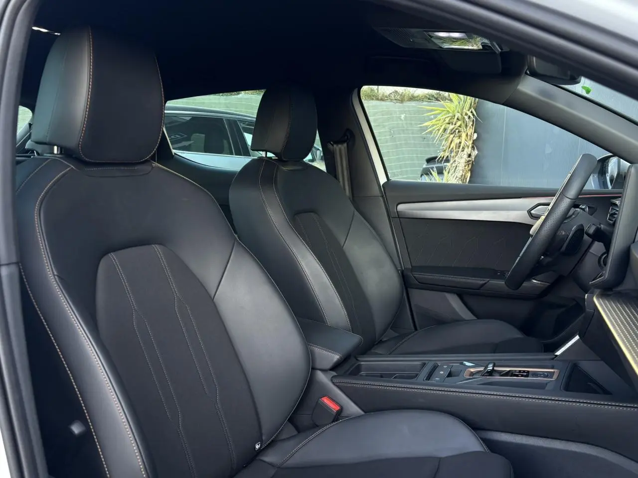 Vue intérieure côté conducteur de la CUPRA Leon 2025 avec sièges sport bimatière noirs et accoudoir central.