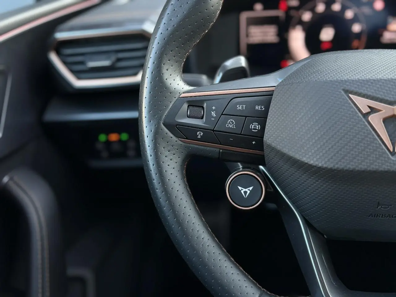 Gros plan sur le volant perforé noir avec logo CUPRA cuivré et commandes multifonctions de la Leon 2025.