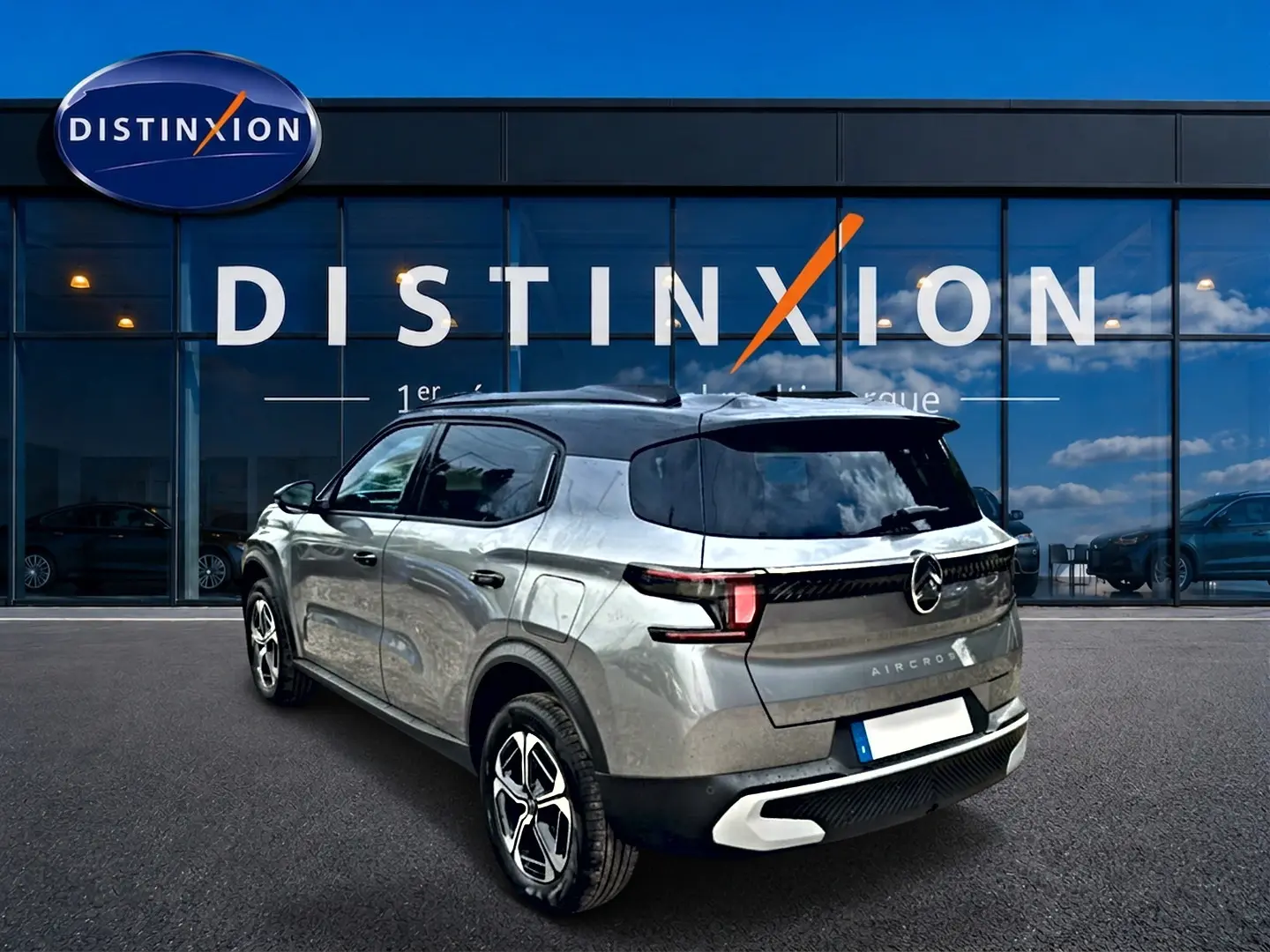 Vue 3/4 arrière droite du Citroën C3 Aircross gris mercury avec toit noir et jantes alu devant un showroom Distinxion.