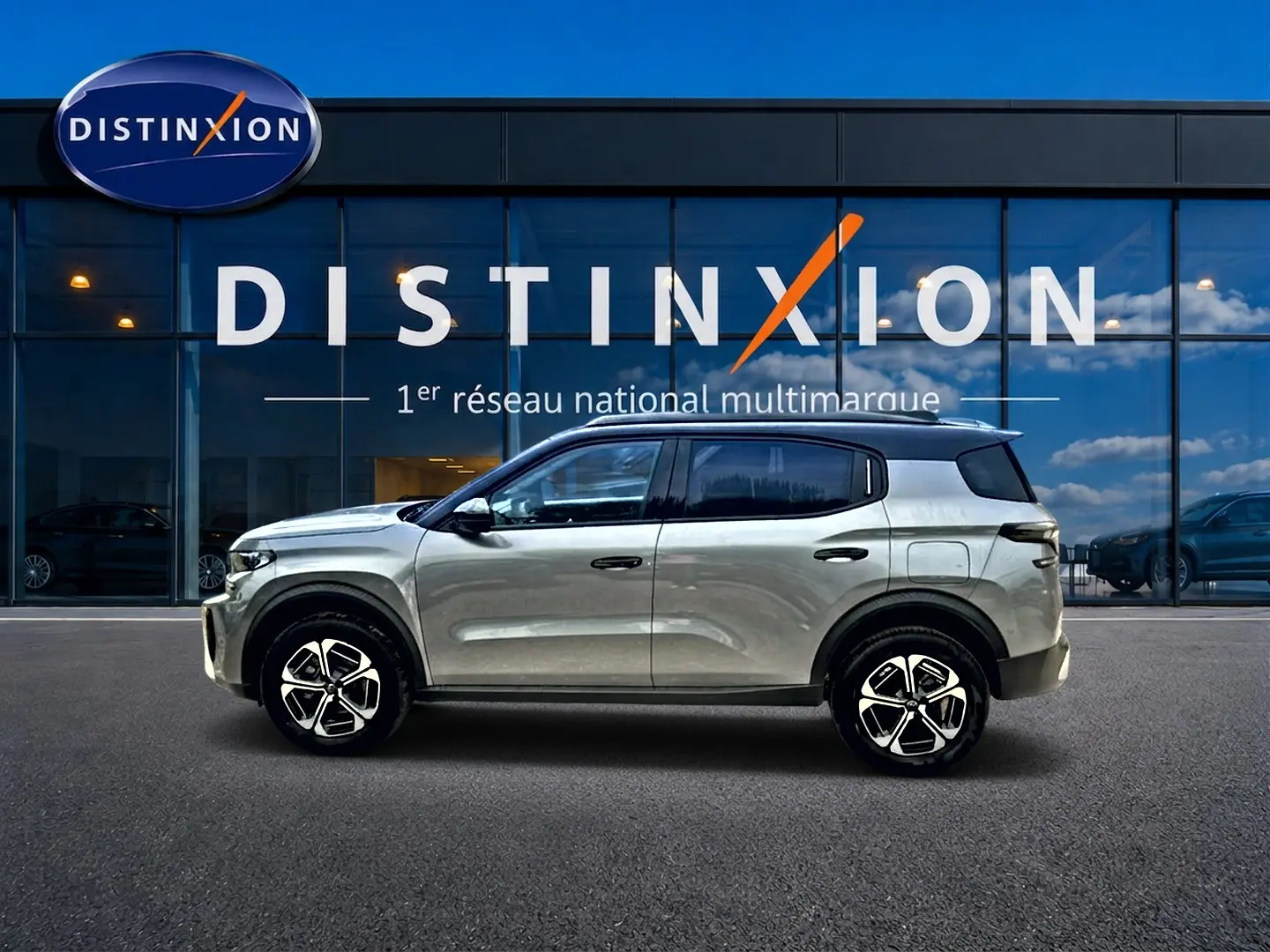 Vue latérale droite d'un Citroën C3 Aircross gris mercury avec jantes alu, devant une vitrine Distinxion.