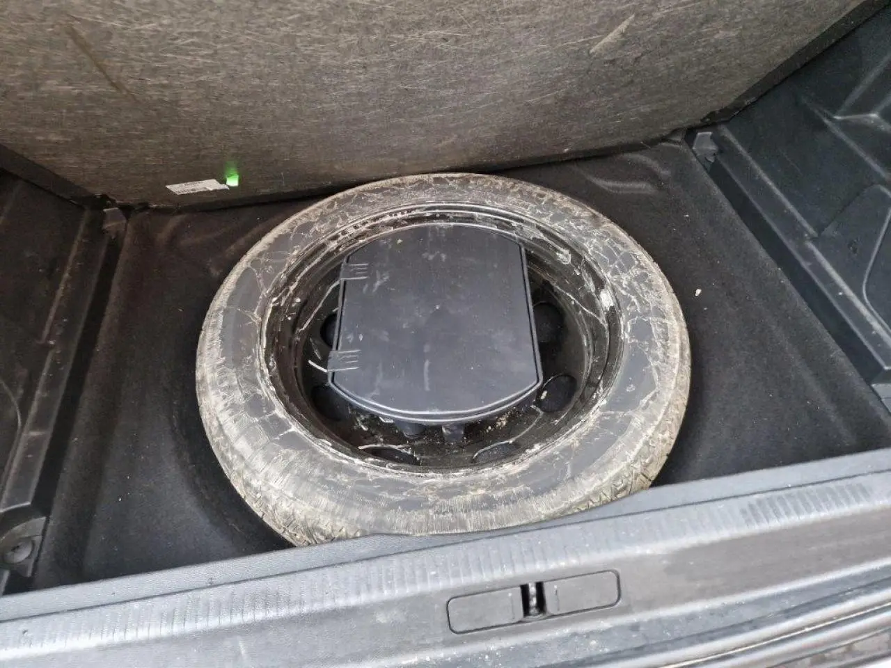 Vue plongeante sur la roue de secours usagée dans le coffre d'un Peugeot 3008 noir 2019.