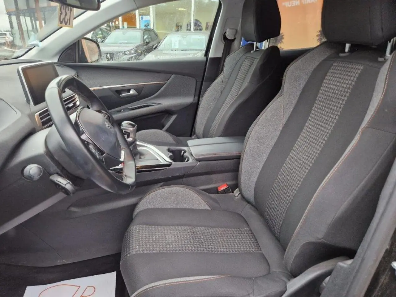 Intérieur avant du Peugeot 3008 noir 2019, sièges tissu gris et noir avec surpiqûres orange, volant cuir multifonctions.