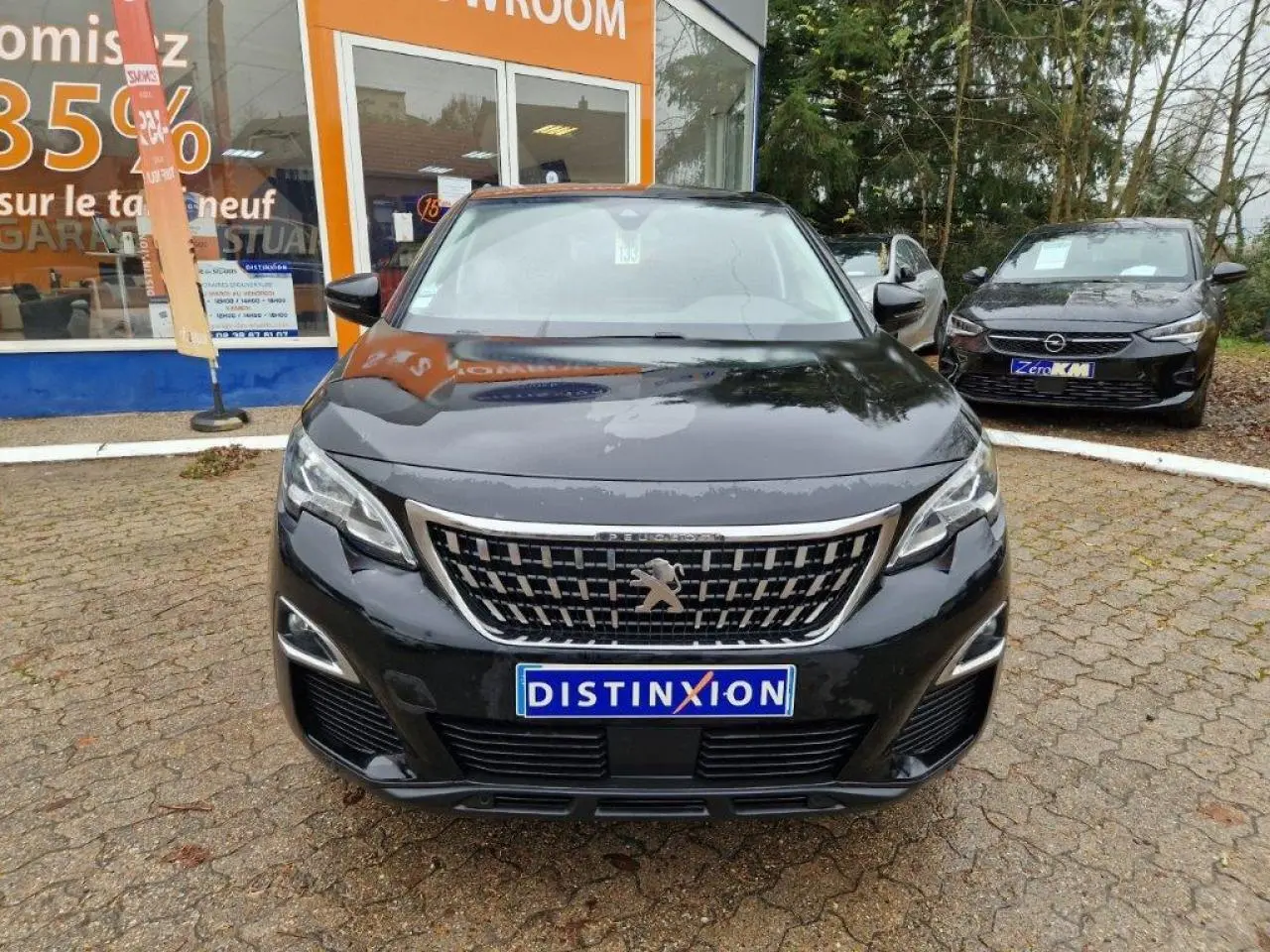 Vue de face d'un Peugeot 3008 noir 2019 avec calandre chromée et plaque Distinxion devant un showroom.