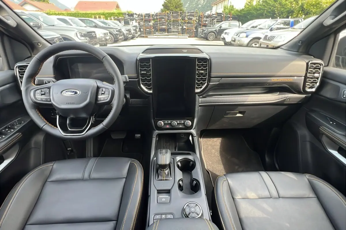 Vue intérieure frontale du Ford Ranger 2.3 PHEV Wildtrak Plus 2025 avec tableau de bord noir et coutures orange contrastantes.