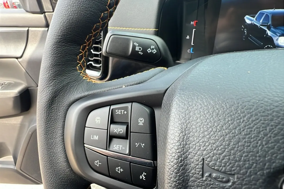 Gros plan sur le volant du Ford Ranger 2025 noir agate, avec commandes intégrées et coutures orange visibles.