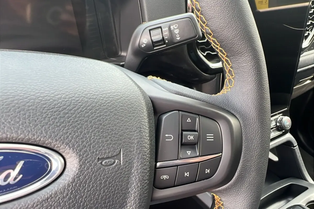 Gros plan sur le volant du Ford Ranger 2025 noir agate, avec surpiqûres orange et commandes intégrées au volant.